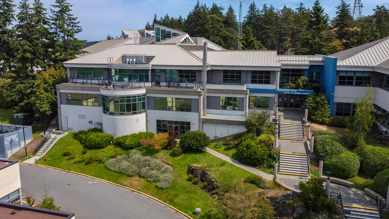 An aerial view of a modern building nestled against huge west coast cedars. There are hills of forest in the background. 